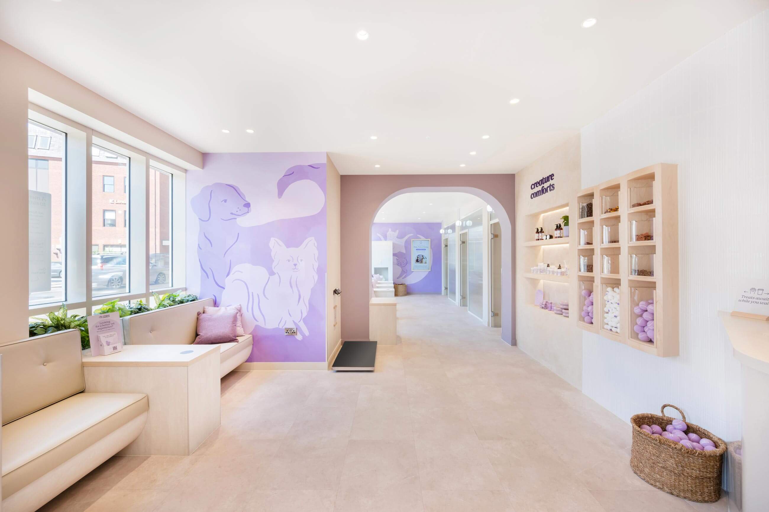 Bright, modern pet care space with light purple accents, cozy seating, and a display of pet products on shelves.